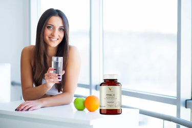 Dziewczyna trzymająca szklankę wody i liposomalną witaminę C Vital C trzymaną na stole