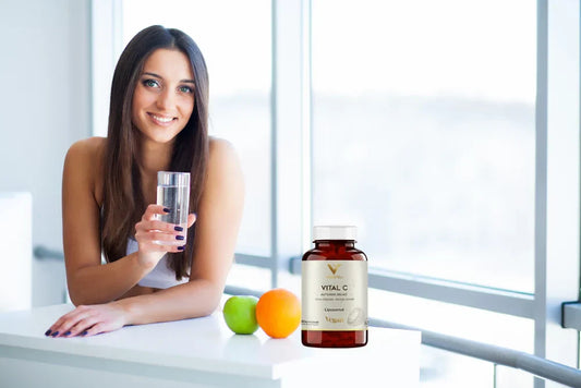 Dziewczyna trzymająca szklankę wody i liposomalną witaminę C Vital C trzymaną na stole