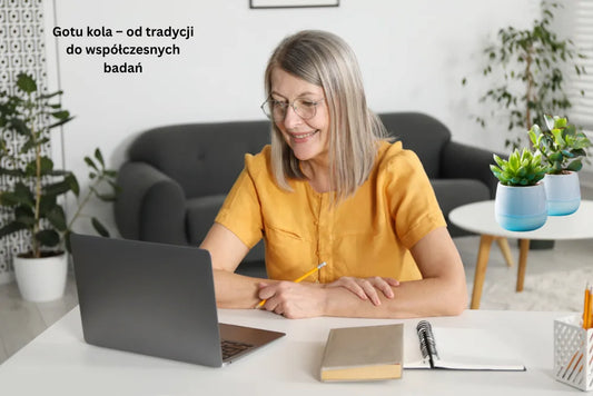 Kobieta siedząca przy stole i pracująca, obok niej szklany wazon z ziołami gotu kola